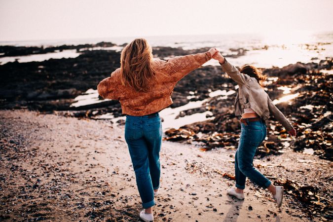 Two young women walking along the beach holding hands high