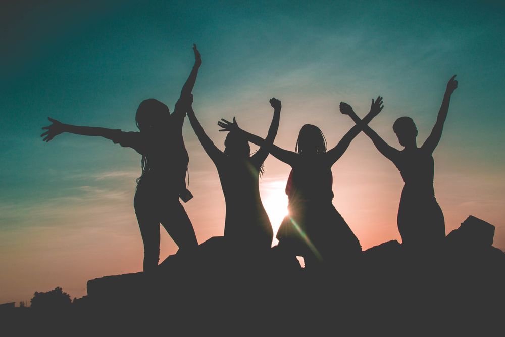 Silhouette of group of women raising their arms at sunset