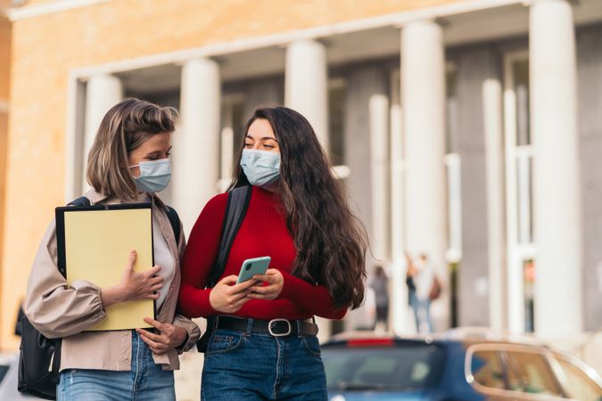 Two students with mask looking the mobile.