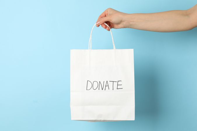 Female hand holds paper bag with inscription Donate on blue background