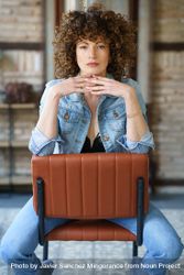 Woman with curly hair sitting on chair reversed resting chin on hands 4BKvXb