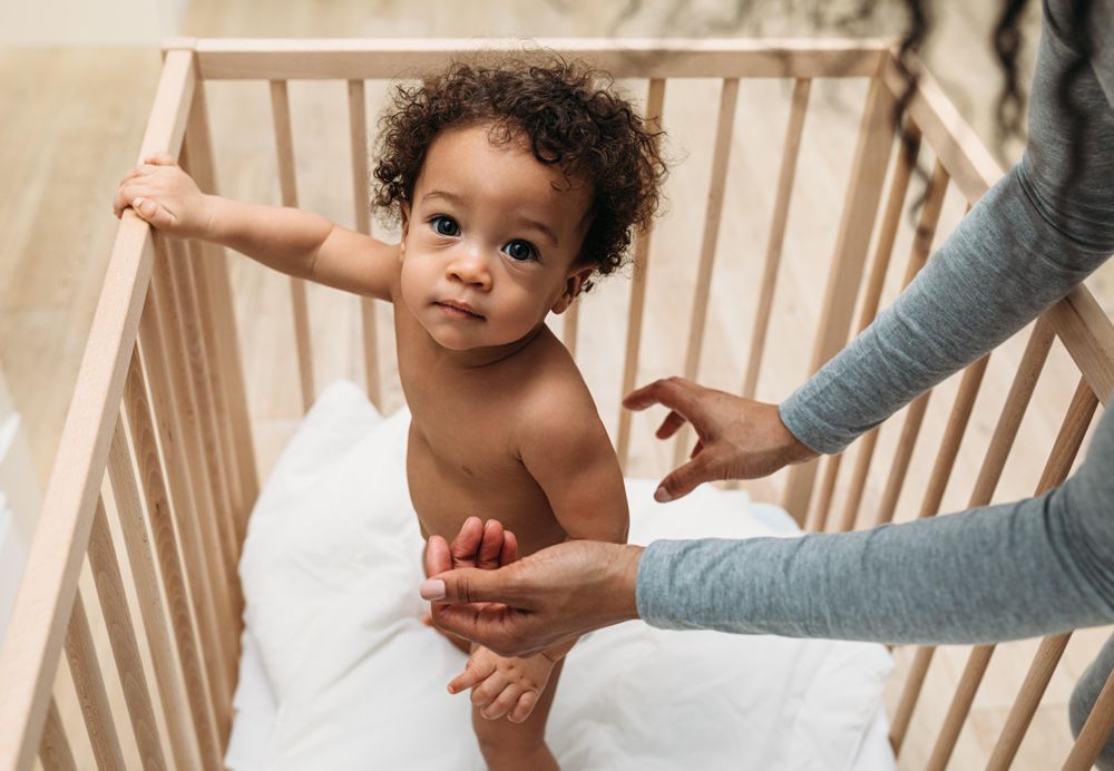 Baby boy standing up with his mother leaning into the crib
