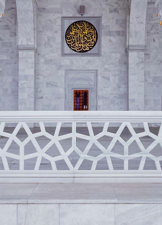 Marble wall in mosque with gold Arabic writing behind fence