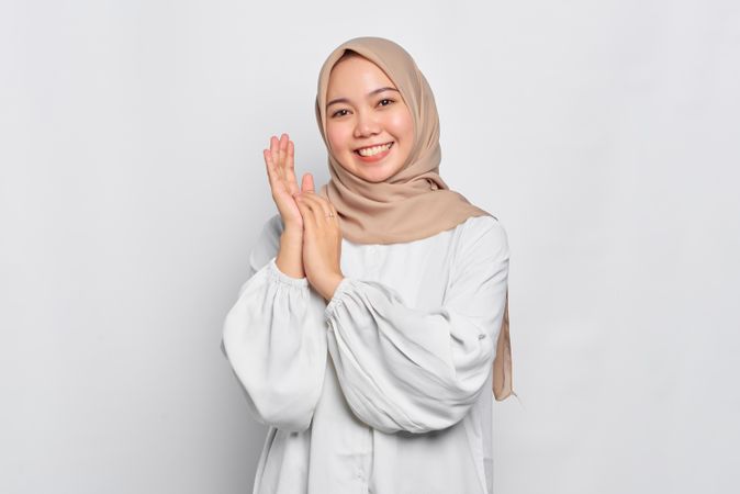 Muslim woman in headscarf and light blouse clapping and smiling
