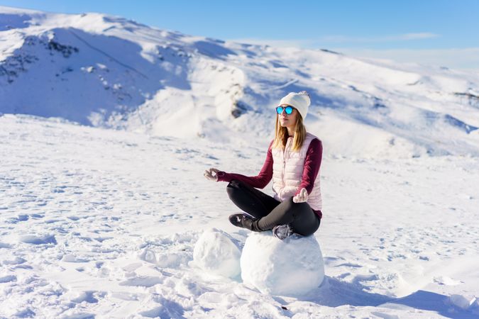 Woman in wintergear meditating on snowy mountain