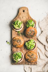 Fresh vegan burgers on seeded buns arranged on wooden bread board