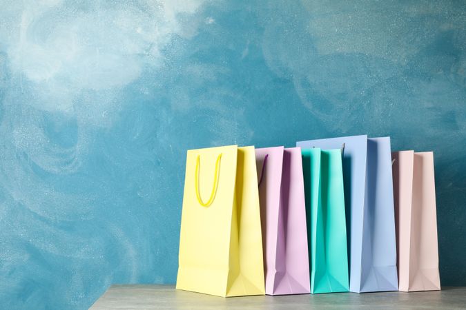 Color bags on grey table against blue background, copy space