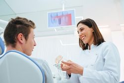 Smiling dentist and assistant showing structure of teeth on prosthesis to client in chair