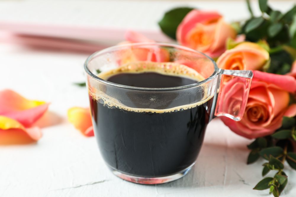 Cup of coffee and pink roses on neutral background, closeup