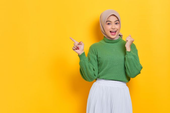 Woman in headscarf pointing at yellow background and making celebratory fist