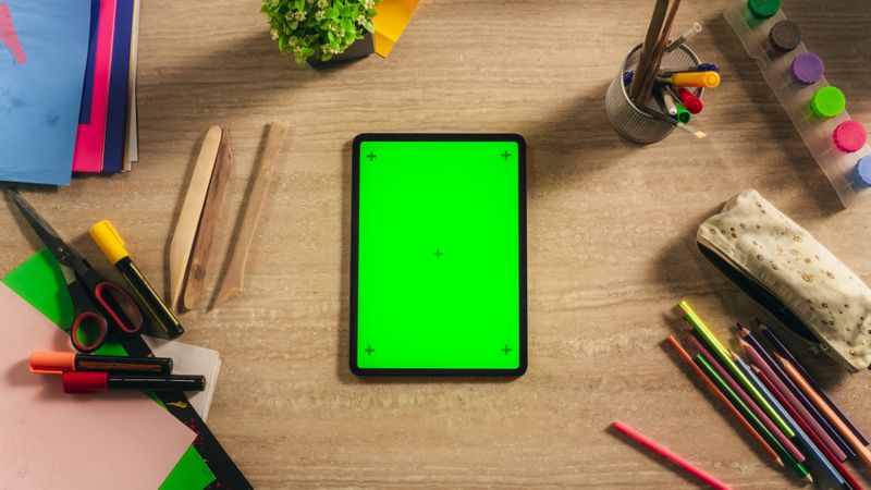 Top View of a Tablet Computer with Vertical Mock Up Green Screen Chromakey Display with Motion Trackers Lying on a Designer's Desk Next to Colorful Pencils, Markers, Art Supply Tools for Illustrators