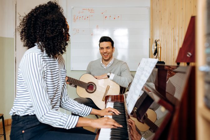 Woman playing piano near man playing guitar in studio