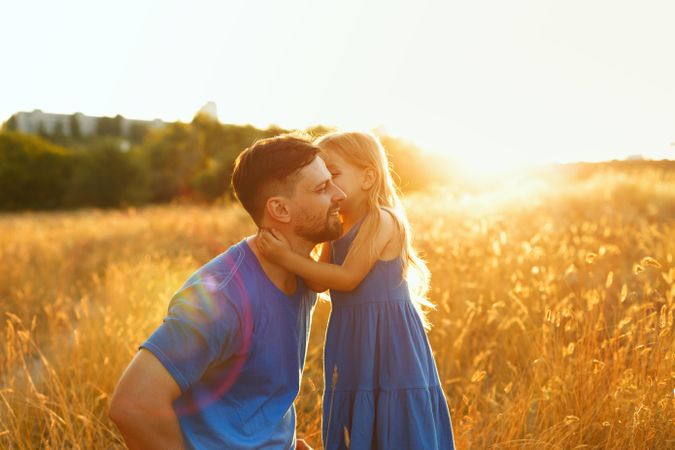 Female child hugs her father in field at sunset