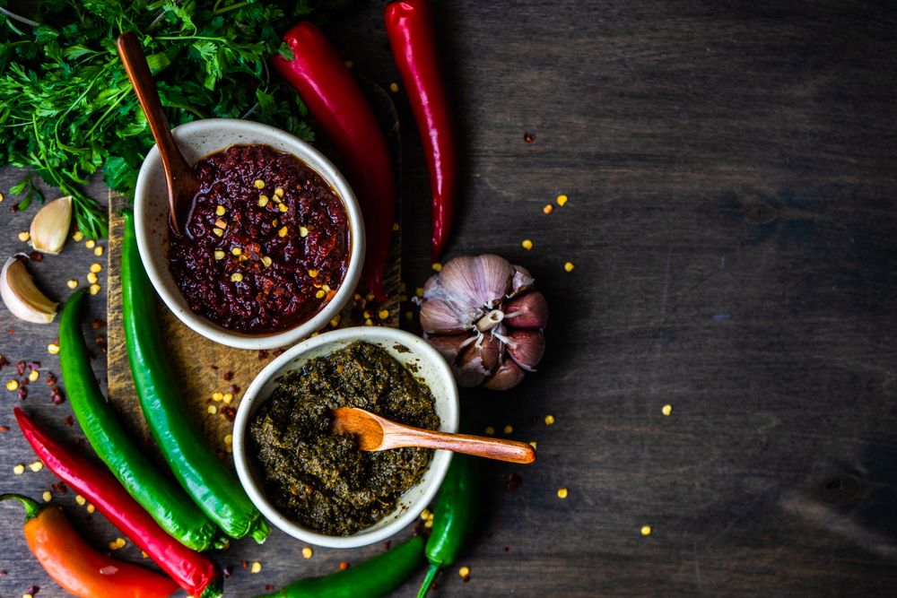 Top view of two rustic pots of traditional Georgian sauce Adjika with garlic bulb and raw ingredients