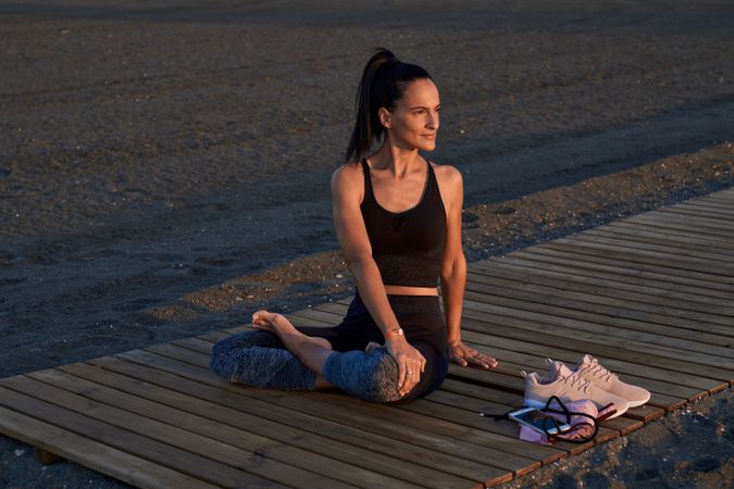 Hispanic woman sitting in Parivritta Sukhasana posture on beach
