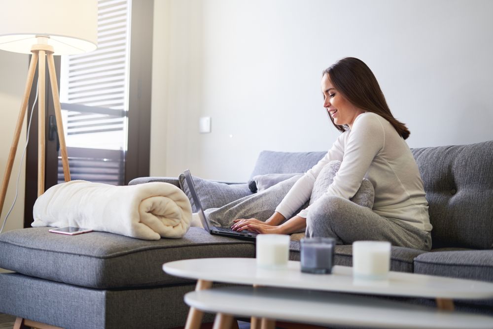 Smiling woman browsing on laptop and sitting on settee