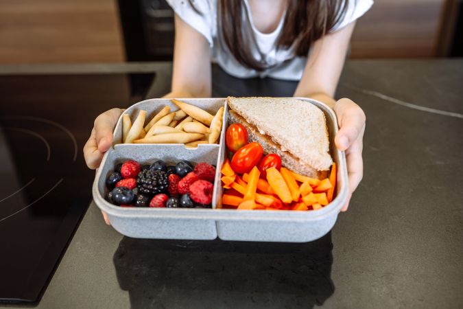 Unrecognizable girl showing lunch box filled with healthy food