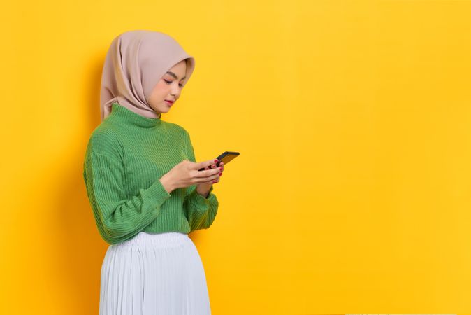 Content woman in headscarf looking down and using her smart phone