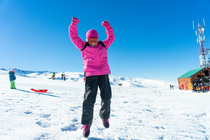 Child in pink snow suit jumping for joy on snowy mountain