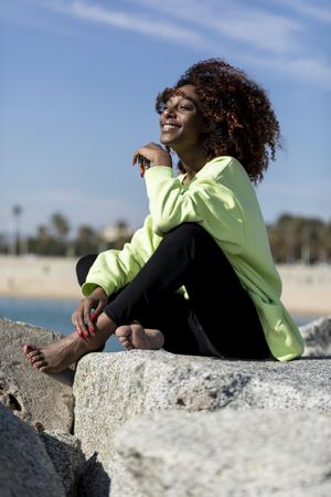 Carefree female in green shirt sitting on rocks near coast