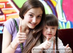 A teenage girl and her younger sister with Down syndrome doing a thumbs up sign 4OKwJ4