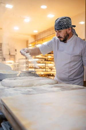 Baker pouring flour on the dough
