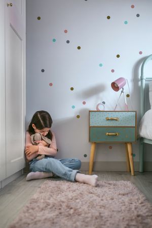 Depressed girl hugging plush doll sitting on the floor