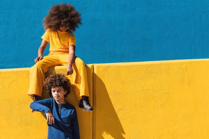 Black curly haired girl and boy resting near colorful wall