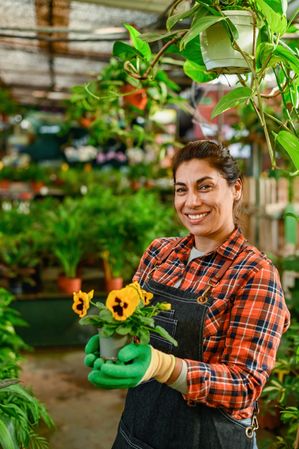 Smiling woman with potted flowers in greenhouse