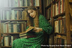 Portrait of girl opening a book while sitting beside bookshelves 5kZrP0