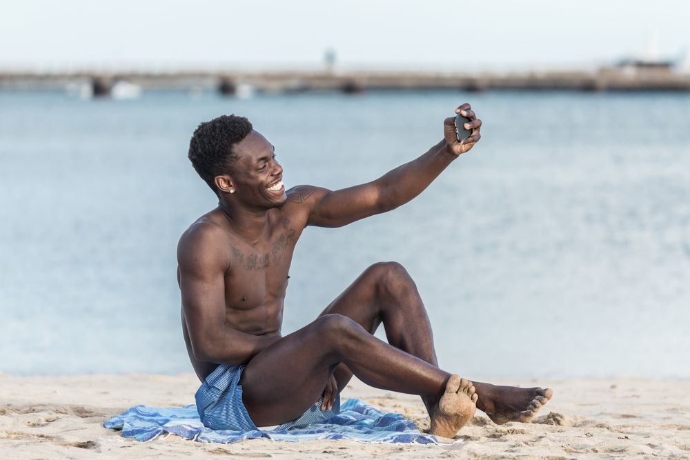 Man sitting on beach taking selfie with his cellphone