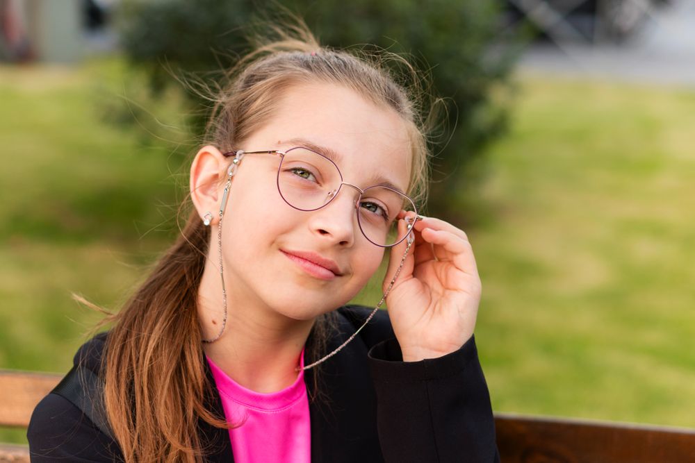 Girl adjusting glasses while sitting on park bench