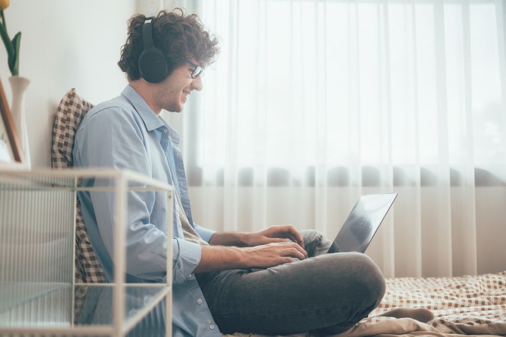 Happy male freelancer listening to music working on laptop