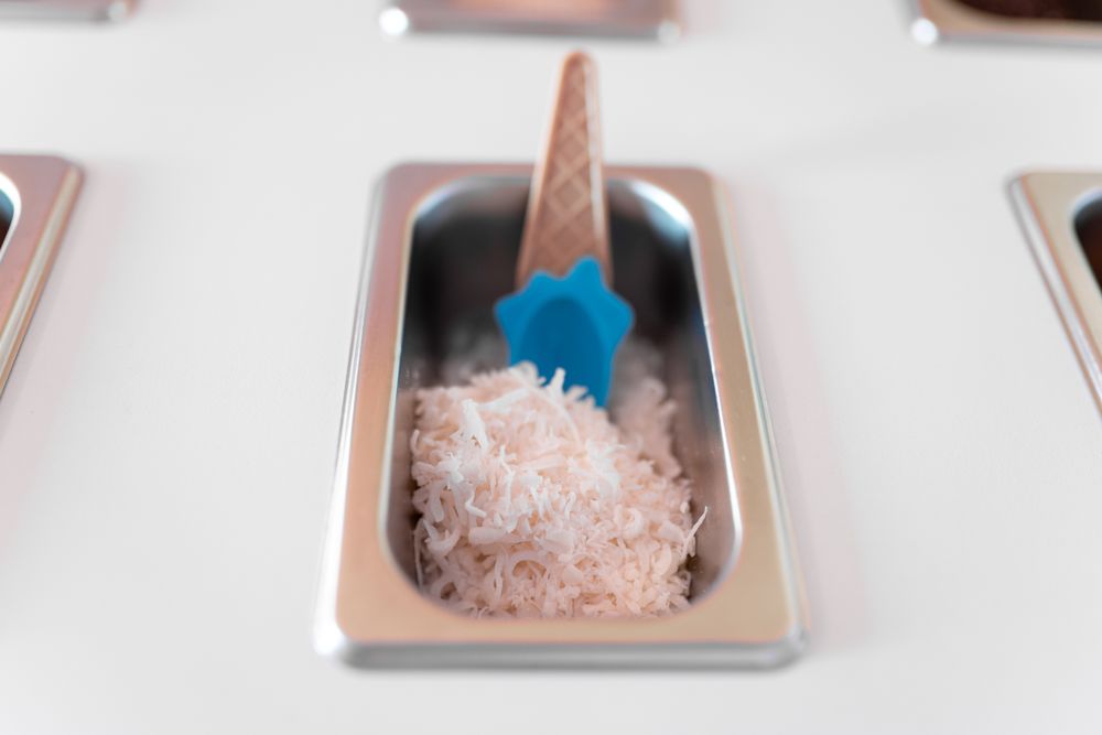 Close up photo of a metal tray filled with striped coconut toppings on an ice cream parlor counter
