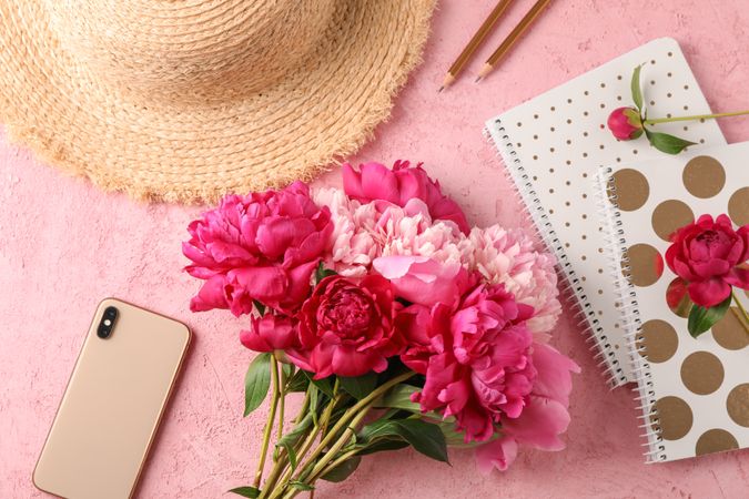 Composition with bouquet of beautiful peonies, straw hat, phone, notebooks and pencils on color background, space for text and top view