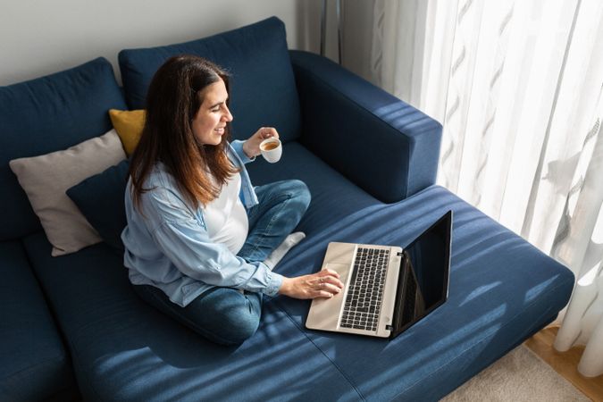 Cheerful pregnant woman drinking beverage on sofa at home