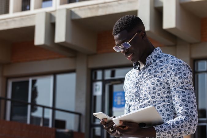 Smiling Black entrepreneur with smartphone and tablet on street