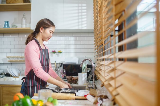 Asian woman in apron washing dishes in the kitchen