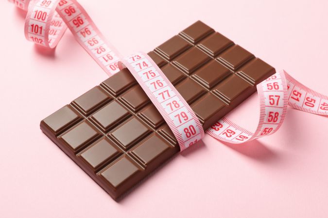 Measuring tape and chocolate bar on pink background
