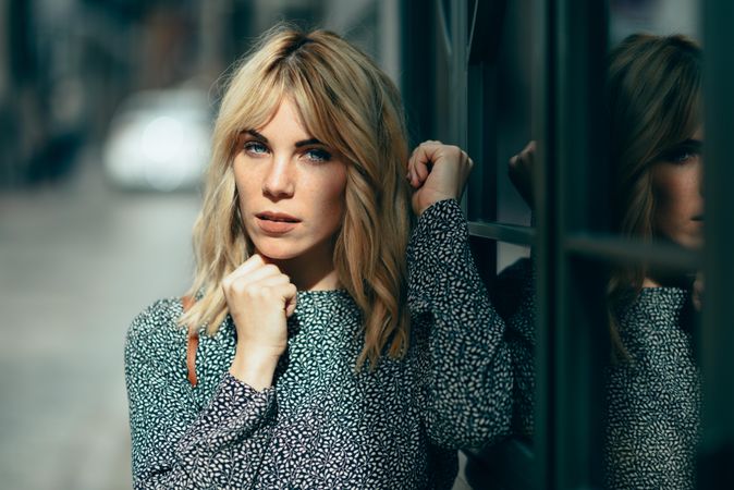 Portrait of blonde female wearing casual clothes standing next to windows outside, copy space