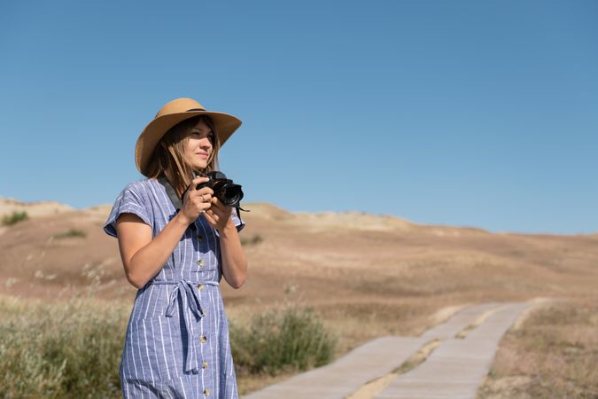 adult woman in straw hat and dress with camera standing on country path
