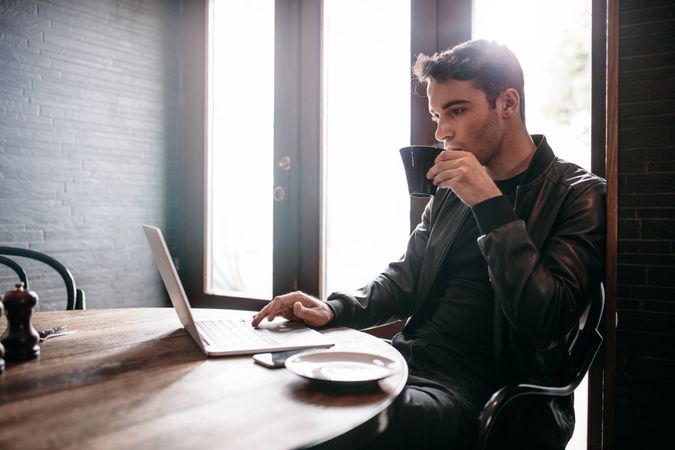 Man sipping coffee in cafe while working on laptop