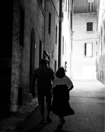Grayscale photo of man and woman walking in an alley
