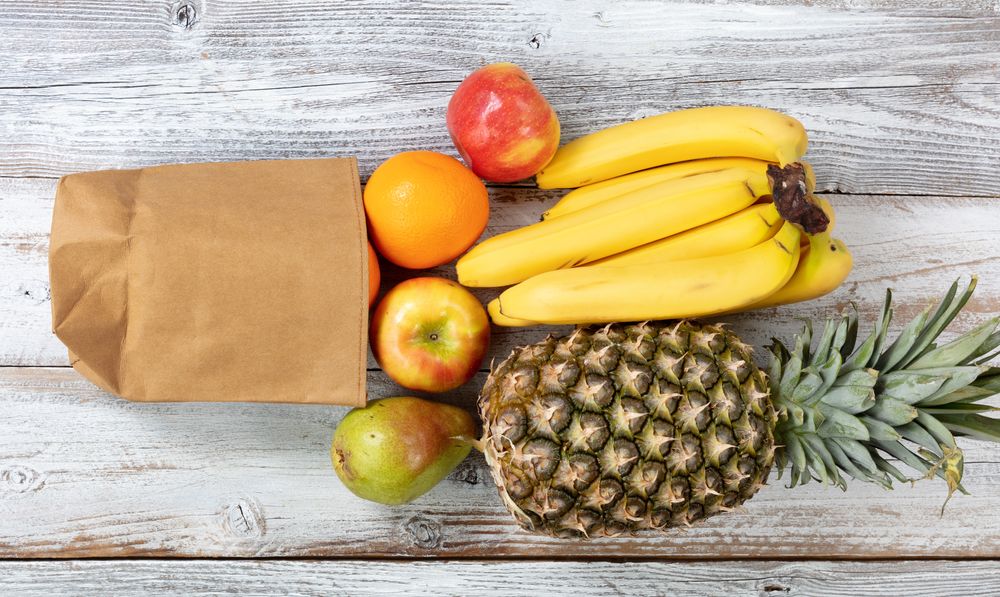 Fresh organic fruit spilling out of recyclable paper bag on rustic wood