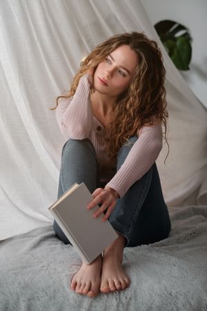 Portrait of young woman sitting on bed and holding book