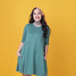 woman in a green dress looking at camera over yellow background.