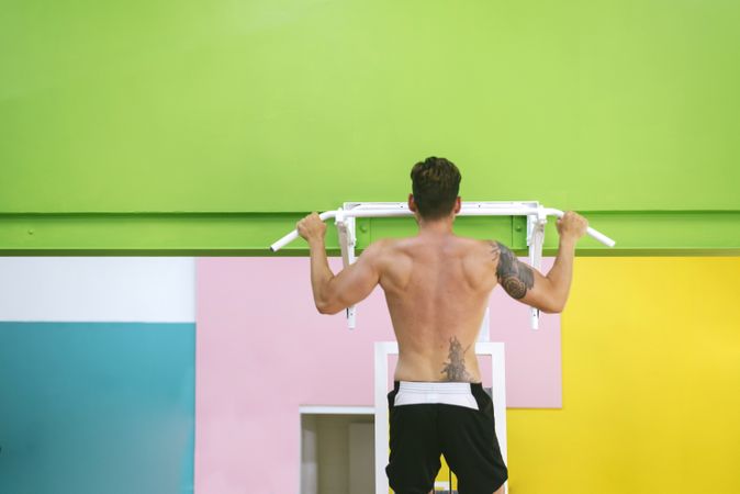 Back of man working out shoulders in a fitness club on pull up bar
