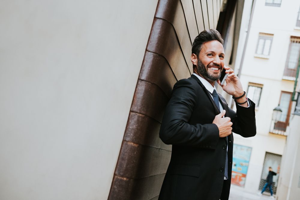 Adult stylish man in costume talking on smartphone near wall