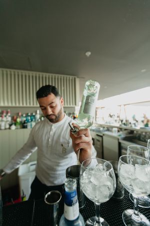 Barman pouring cocktail and alcoholic drinks to shaker in a bar.