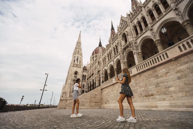 Stylish women taking photos on square against old building